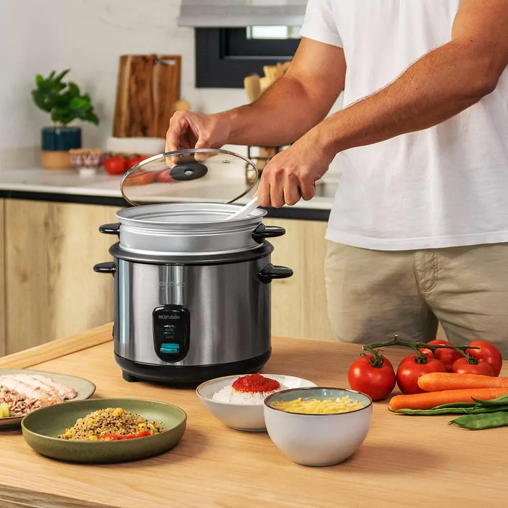 Hombre utilizando la arrocera cecotec en un encimera rodeada de diferentes alimentos puestos en platos y tazones.